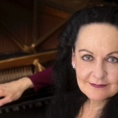 Pianist Sarah Grunstein, leaning her hand on a grand piano.