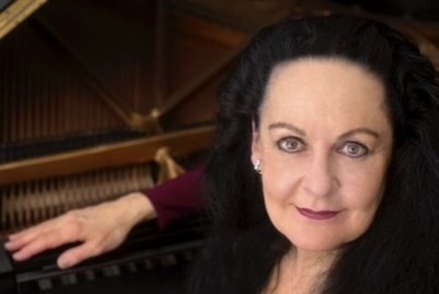 Pianist Sarah Grunstein, leaning her hand on a grand piano.