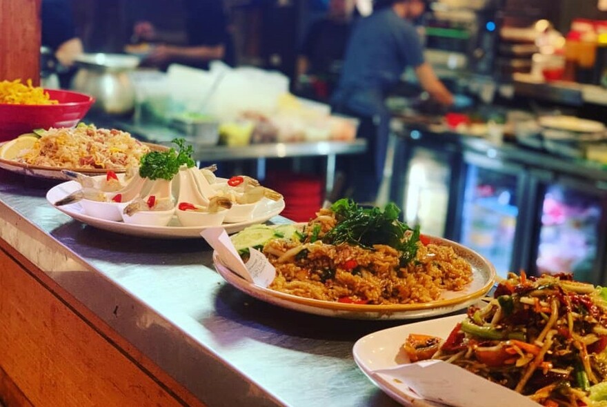 Plates of Thai food lined up on kitchen counter.