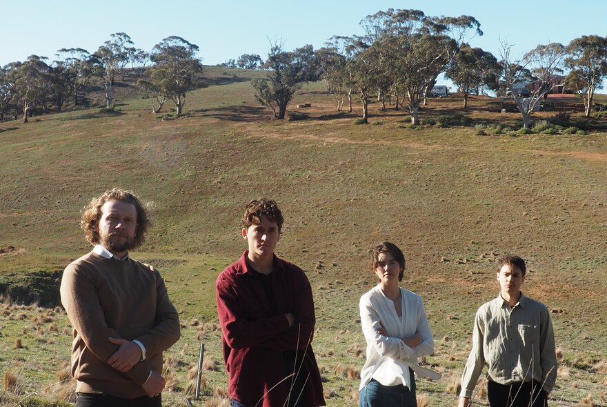 Four people with arms crossed standing in a barren landscape with trees.