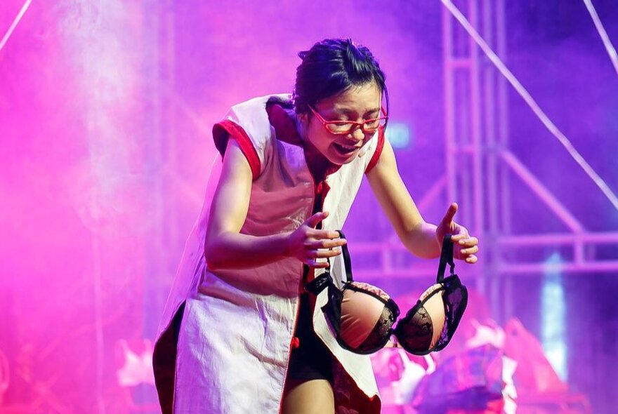 Performer holding a bra while performing against purple lights.