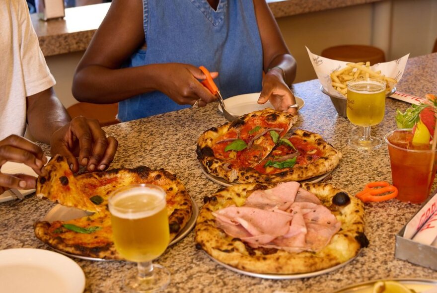 Customer slicing her pizza up with scissors at a table set with pizzas and drinks.