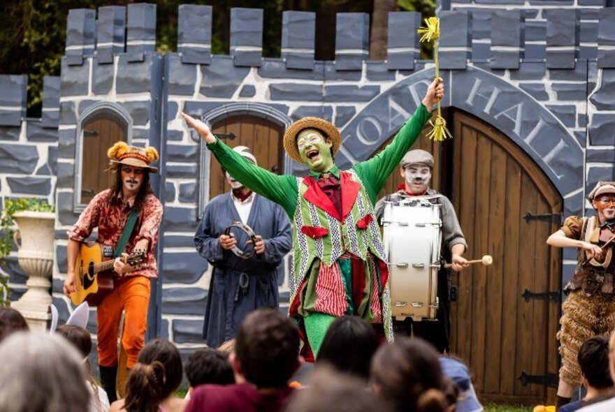 A group of actors dressed as Wind in the Willows characters performing outdoors in front of a mock castle.