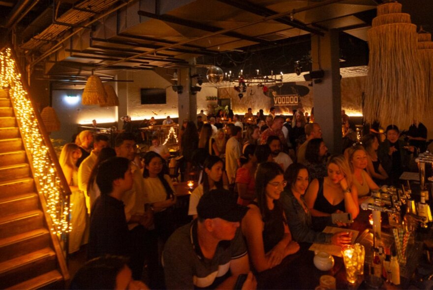 The inside of a dimly lit venue with patrons lining up at the bar for drinks.