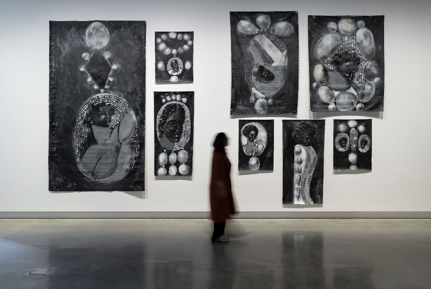 Black and white artworks on white gallery wall, a person silhouetted against the white.