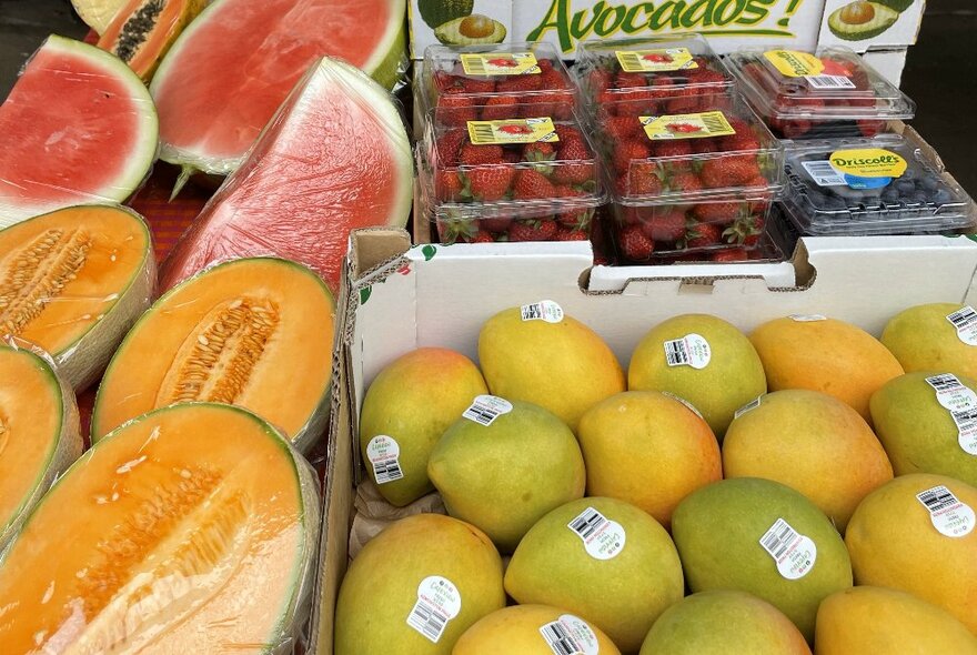 Boxes of fruit including halved canteloupes, mangoes and berries.