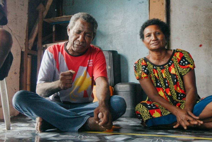 Two people from Papua New Guinea sitting cross-legged on a floor.