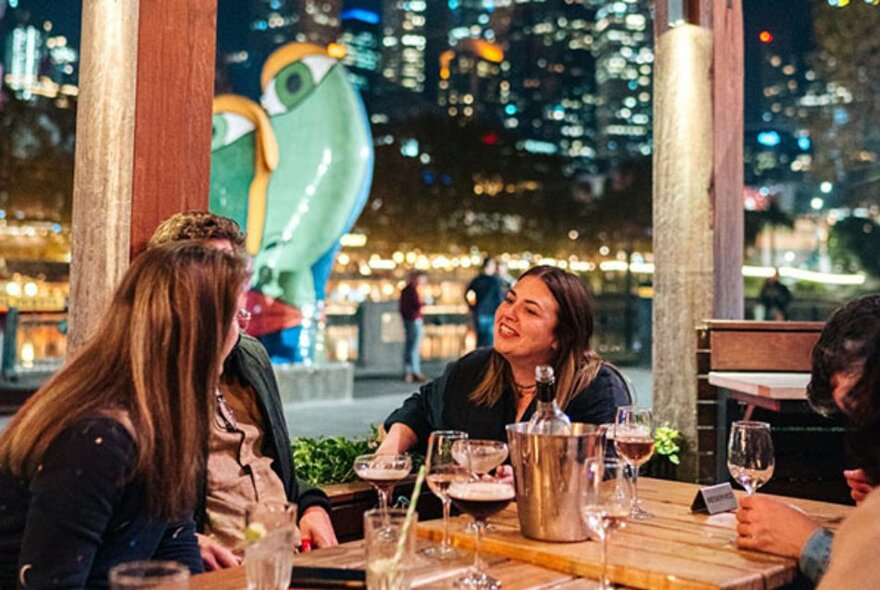 Diners at an indoor venue overlooking the river with city lights in the background.