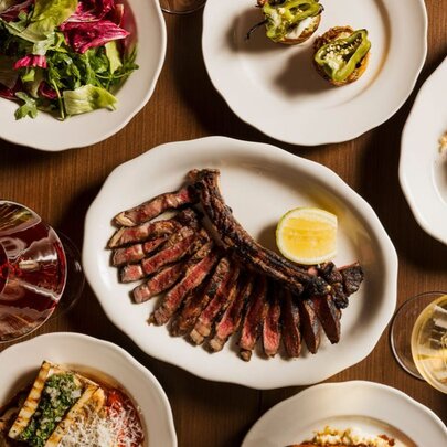 A table spread featuring a central plate of sliced steak with a lemon wedge, surrounded by multiple dishes.