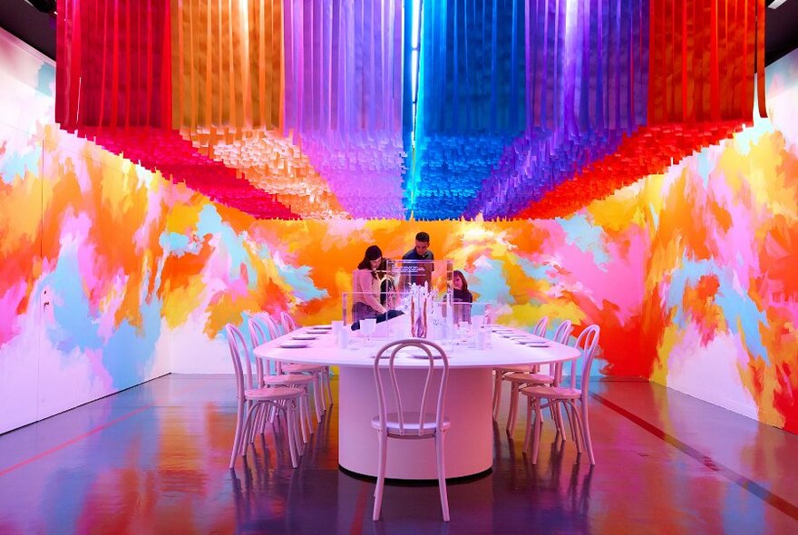 A family standing around a large pink table in a colourful gallery exhibition.