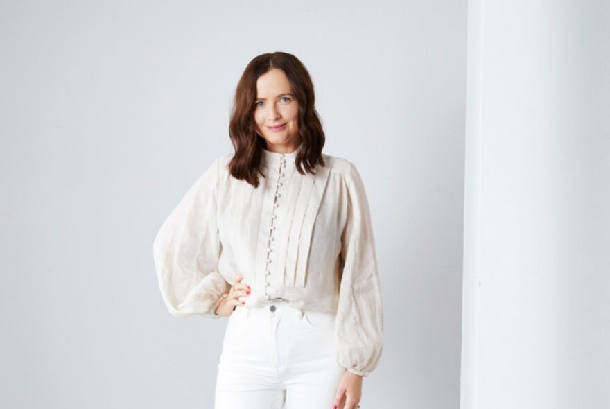 Woman wearing a white blouse and trousers, her hand on her hip.