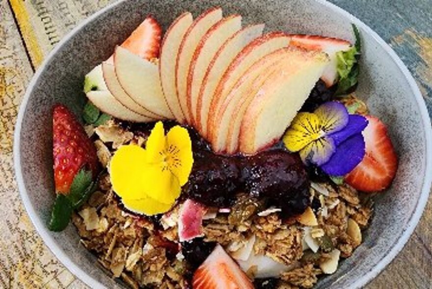 A bowl of granola topped with fruit and pansies.