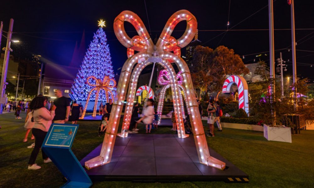 Child swinging on a swing under a giant lit up Christmas bell.