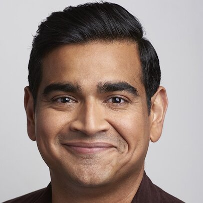 Smiling face of comedian Dilruk Jayasinha, a middle aged man with dark hair, against a neutral background.