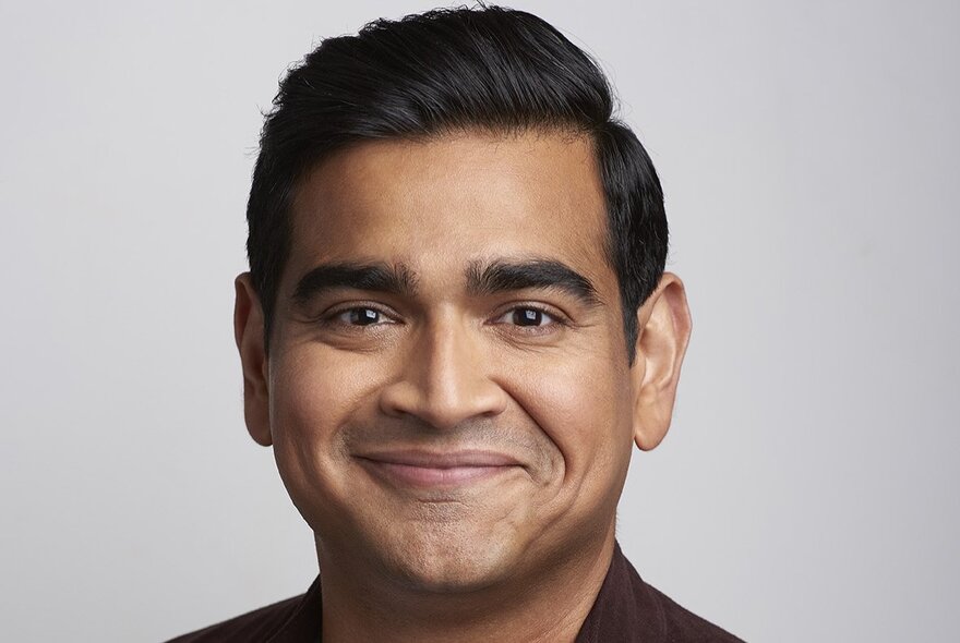 Smiling face of comedian Dilruk Jayasinha, a middle aged man with dark hair, against a neutral background.