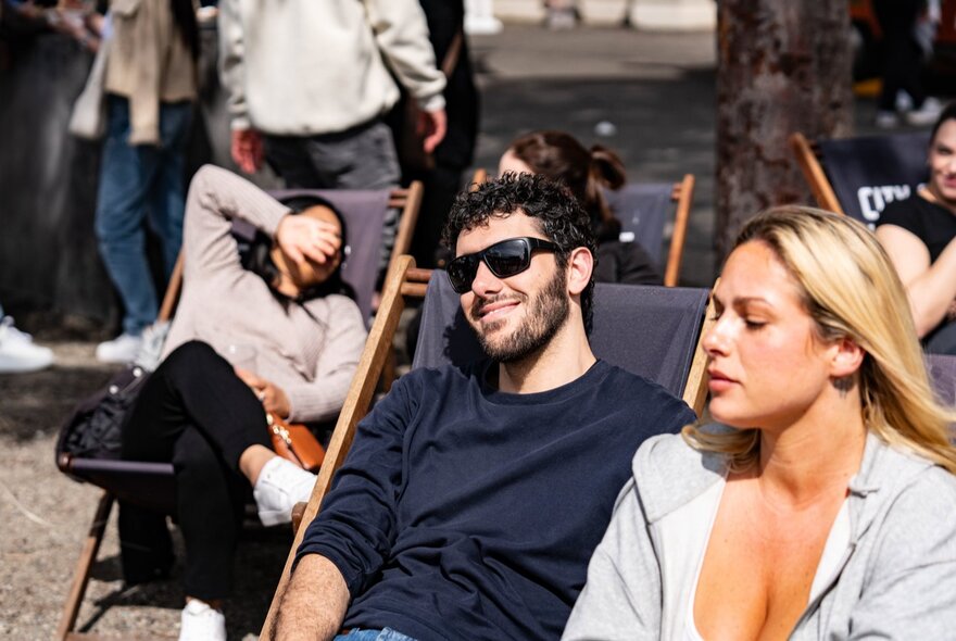 Three people enjoying the sunshine in deck chairs, one holding her hand over her face to shield her eyes.