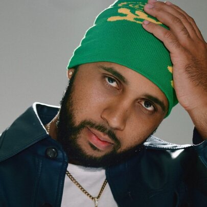 Indigenous man holding his hand to his green hat.