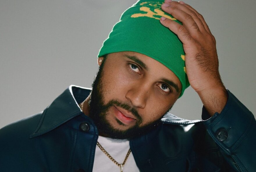 Indigenous man holding his hand to his green hat.