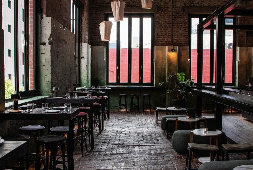 Interior of Longsong bar showing cobbled floor, small tables and chairs perched near large windows, hanging lanterns and greenery.