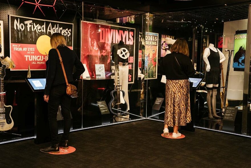 Museum visitors standing at display consoles surrounded by posters and artefacts.