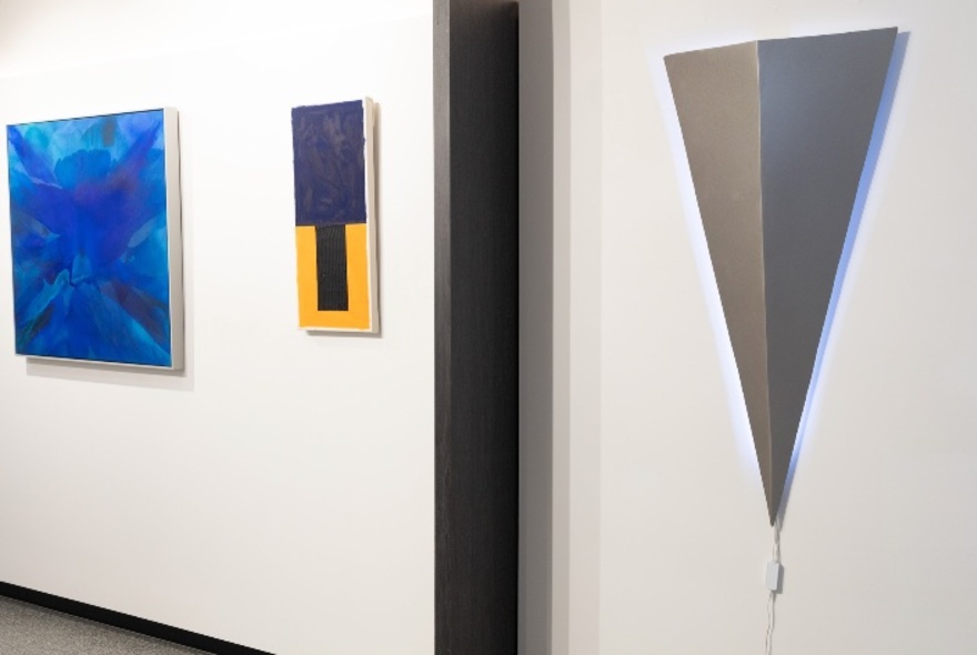 White gallery walls hung with abstract artworks including a grey triangle and blue painting.