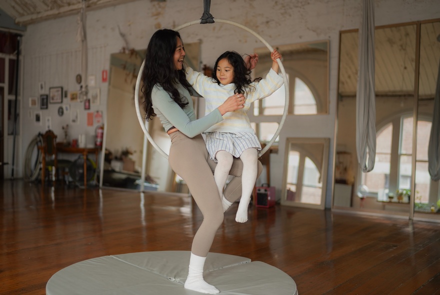 Adult and child seated on a circular swing in a studio setting.