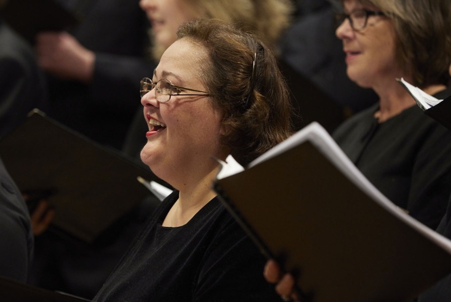 Choir performers wearing black, singing from black songbooks.
