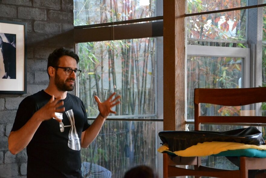 Edwin Fox presenting a talk, with a mid-century dining chair on display in a room with an exposed brick wall and windows overlooking bamboo. 