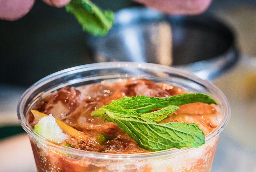 A cold drink in a glass being garnished with fresh mint leaves.