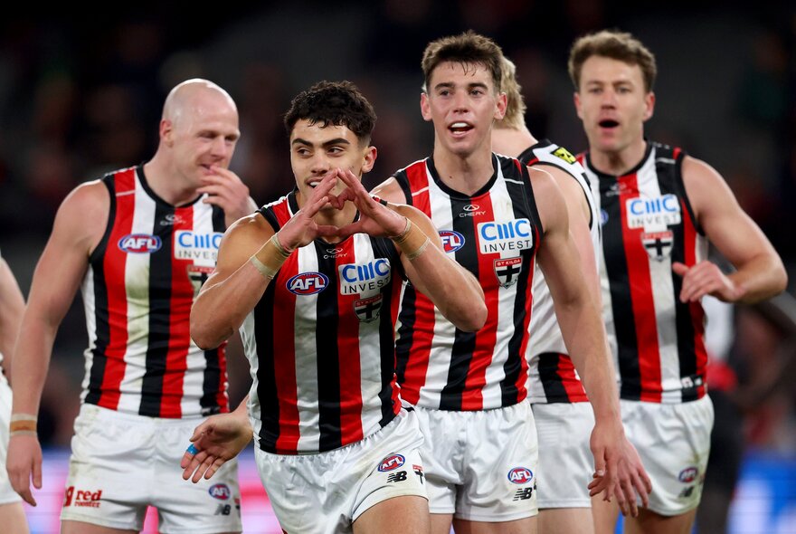 St Kilda football players running together during a match, looking happy. 