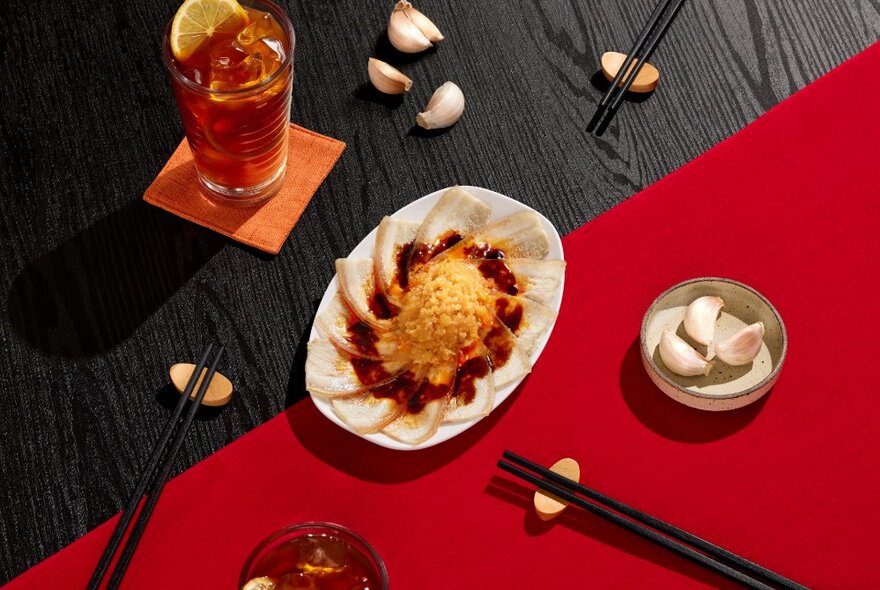 Looking down on a table set with chopsticks on rests, garlic and a noodle dish. 