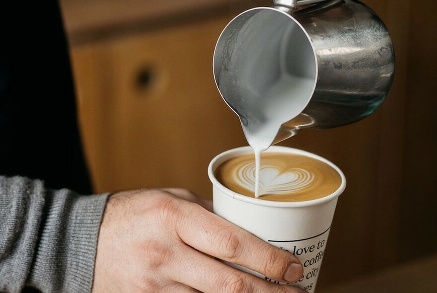 Person creating latte art on a takeaway coffee cup.