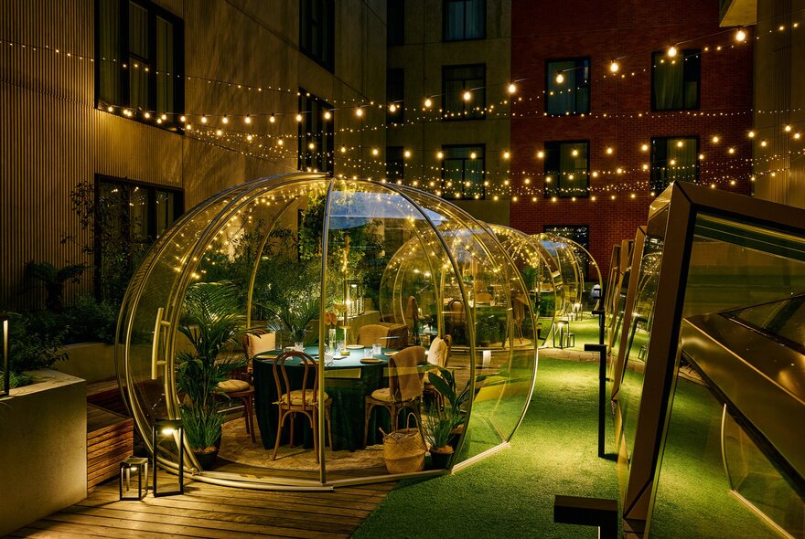 A rooftop garden at night with transparent igloos and string lights hanging from above