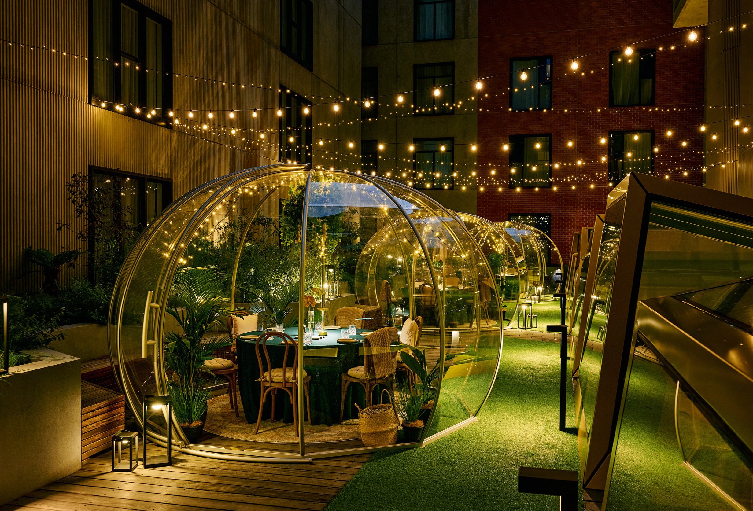 A rooftop garden at night with transparent igloos and string lights hanging from above