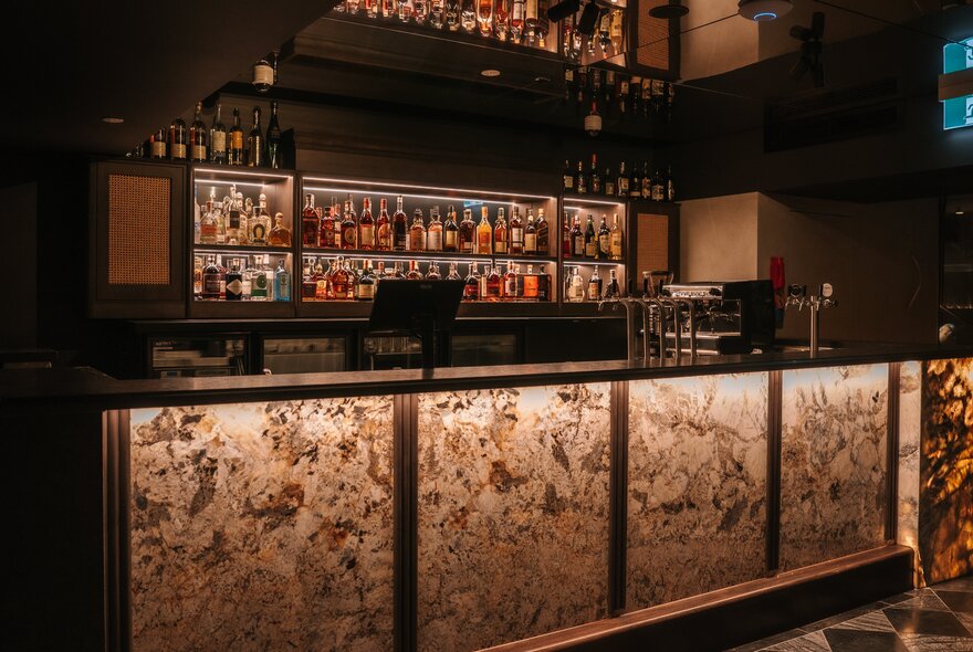 A dimly lit bar with rows of spirits behind.