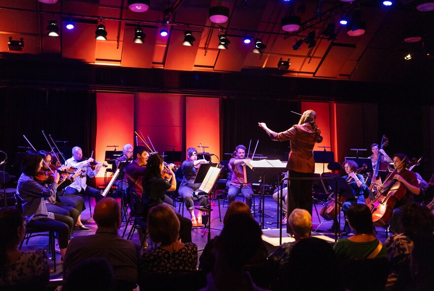 Orchestra Victoria performing in a small space with dim lights glowing purple and red. 