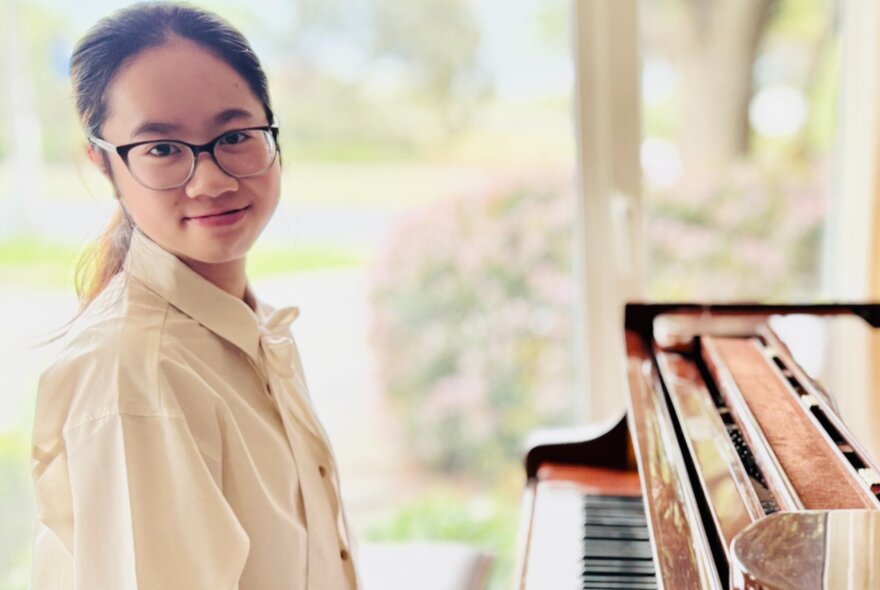 Musician Jasmine Lai seated at a piano with blurred garden view in the background.