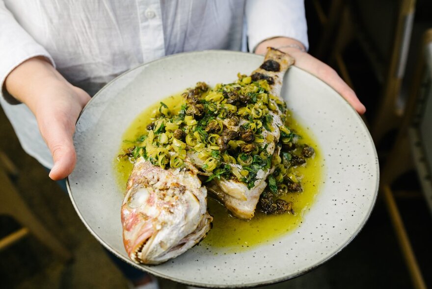 A plate of whole red snapper with a thai-style sauce, being held by a waitress in a white shirt.