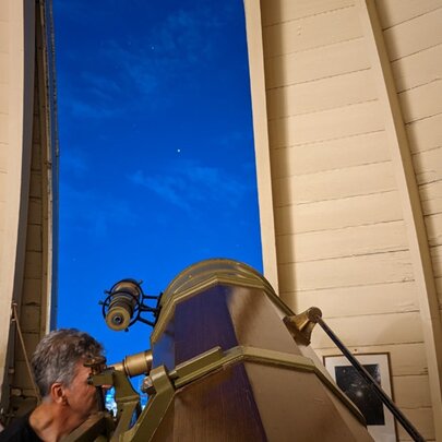 A man looking into the eyepiece of a large telescope, pointed towards the night sky at the Melbourne Observatory.