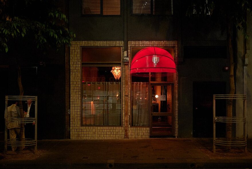 A glowing red street canopy over a dark doorway in a laneway.