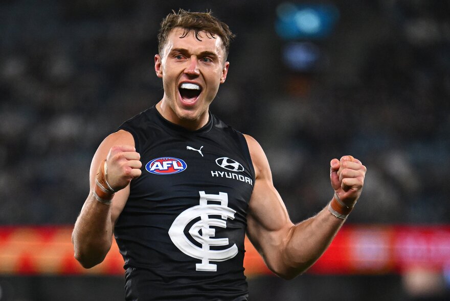A Carlton AFL football player with his fists clenched and pumped up during a match.