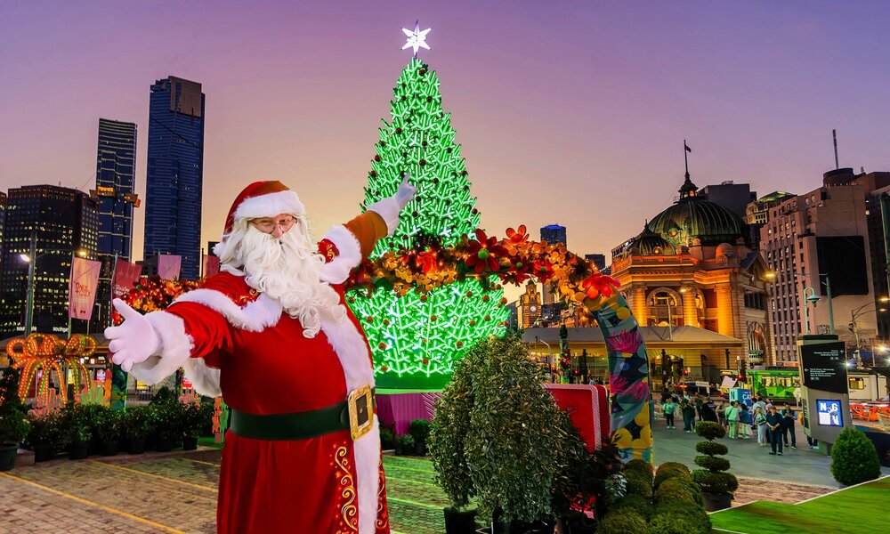 Santa in front of a lit up Christmas tree in Fed Square. 