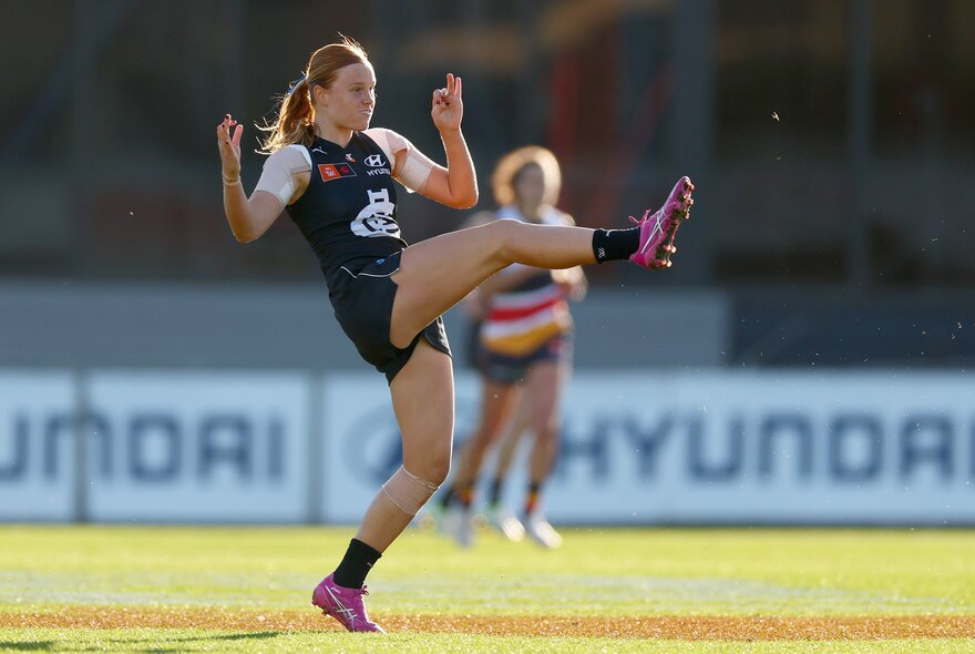 A Carlton AFLW player directly after kicking a football, leg still in the air. 