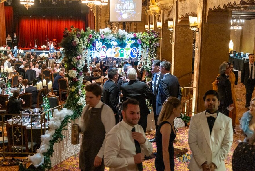 Wait staff in a formal dining area with tables of diners in the background.