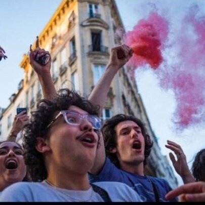A crowd of people with pink powder flares in a city setting
