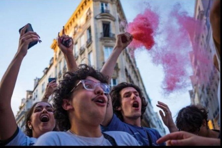 A crowd of people with pink powder flares in a city setting