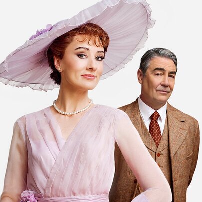 A scene from the musical My Fair Lady with Eliza Doolittle in a pink dress and hat and Henry Higgins in a tweed three-piece suit. 