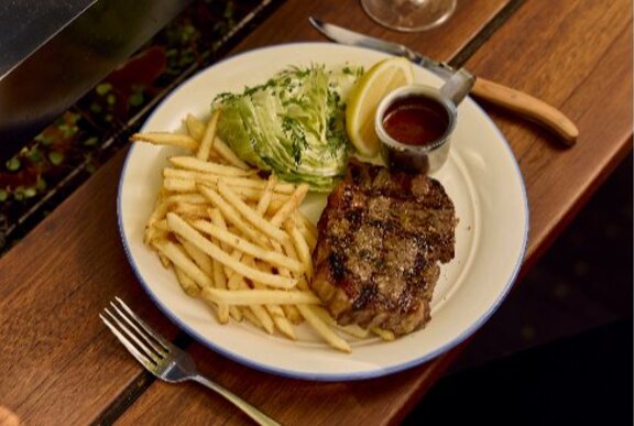 Plate of steak and chips with salad and sauce, with cutlery.