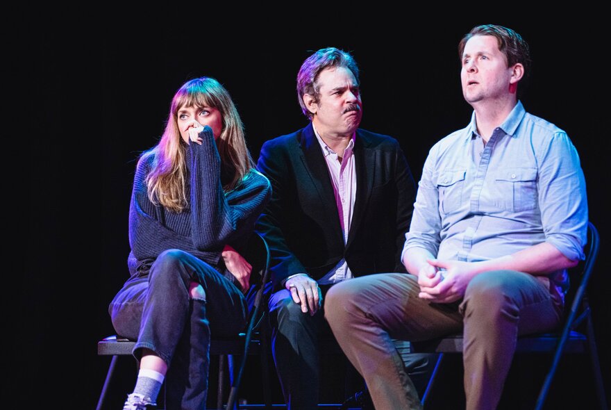 Three performers seated on stools on a stage in front of an audience, improvising a scene.