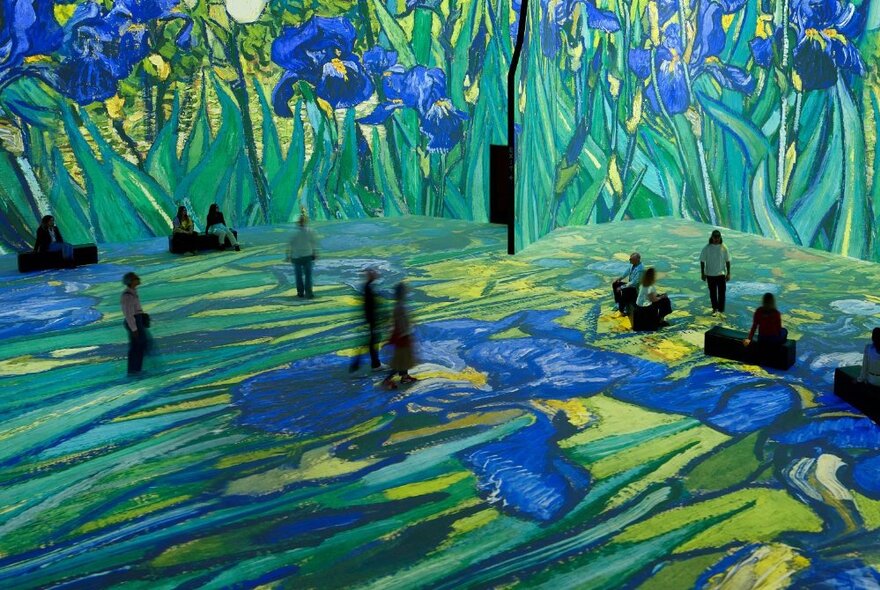 People walking around a very large exhibition space with Vincent van Gogh's paintings if blue iris flowers digitally projected on all the wall and floor spaces.